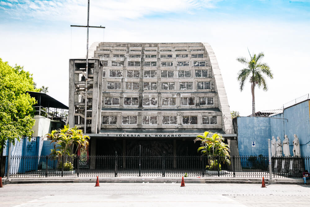 Overal in Centraal Amerika kom je kerken tegen. Maar de kerk Iglesia el Rosario in het centrum van San Salvador is een van de bezienswaardigheden die je niet mag missen vanwege haar bijzondere architectuur en stijl. Wat vanuit de buitenkant een grijze betonnen loods lijkt, doet je aan de binnenkant verwonderen aan design, kleuren en lichtval.