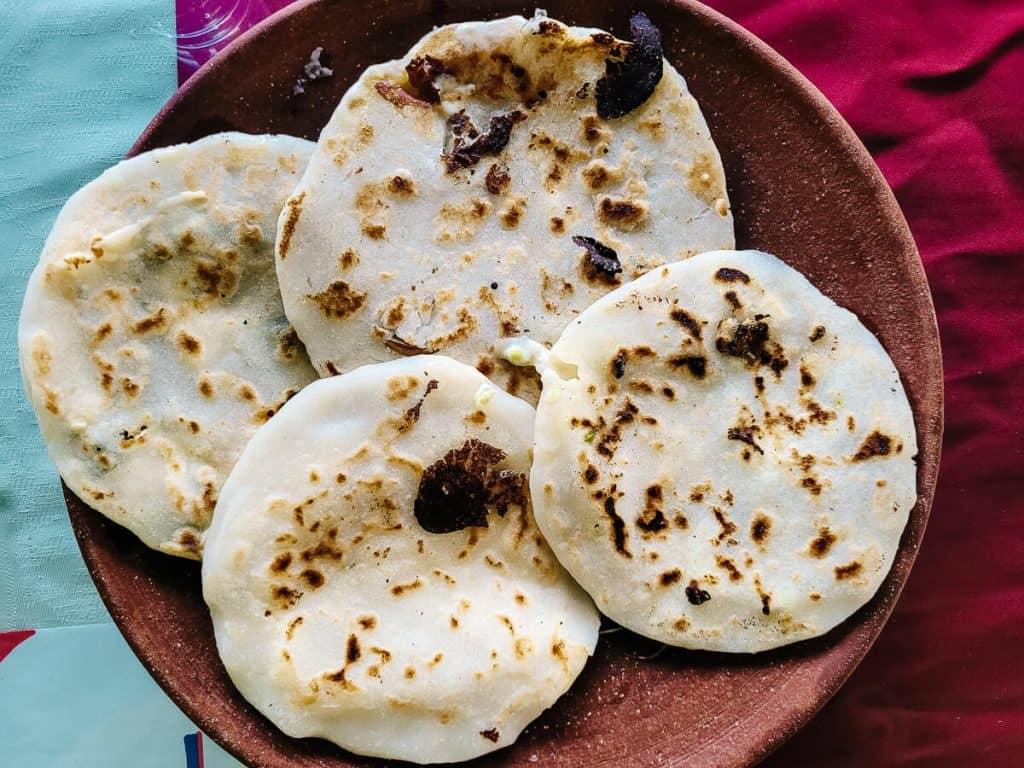 A pupusa is a type of flatbread, made with cornmeal or rice flour. It is filled with ingredients that you choose yourself, such as cheese, beans, chicken, meat, loroco, pumpkin and much more. And you eat it together with curtido (a fermented coleslaw) and sauce and of course with your hands.
